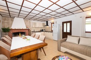 A modern kitchen with a brick fireplace, white cabinets, and a dining area with a wooden table and chairs. - House Mario (Supetar)