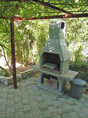 An outdoor brick oven with a chimney, located on a paved patio surrounded by bamboo plants. - Apartment Renci (Biograd na Moru)