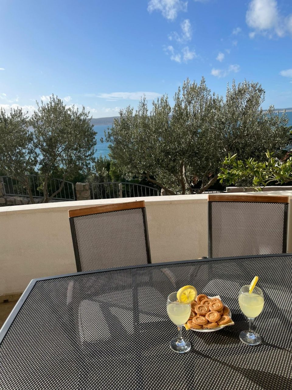 Een tafel met uitzicht op zee, een bord gebakjes en twee glazen geel drank.