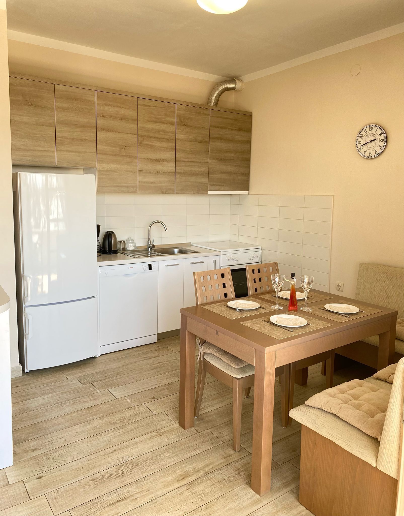 Une cuisine compacte équipée d’un réfrigérateur, d’une cuisinière, d’un évier et de meubles de rangement en bois. On peut également apercevoir une table à manger avec des chaises et un canapé.