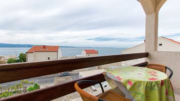 Un balcón con sillas de mimbre y una mesa, con vistas a la costa, edificios y una carretera.