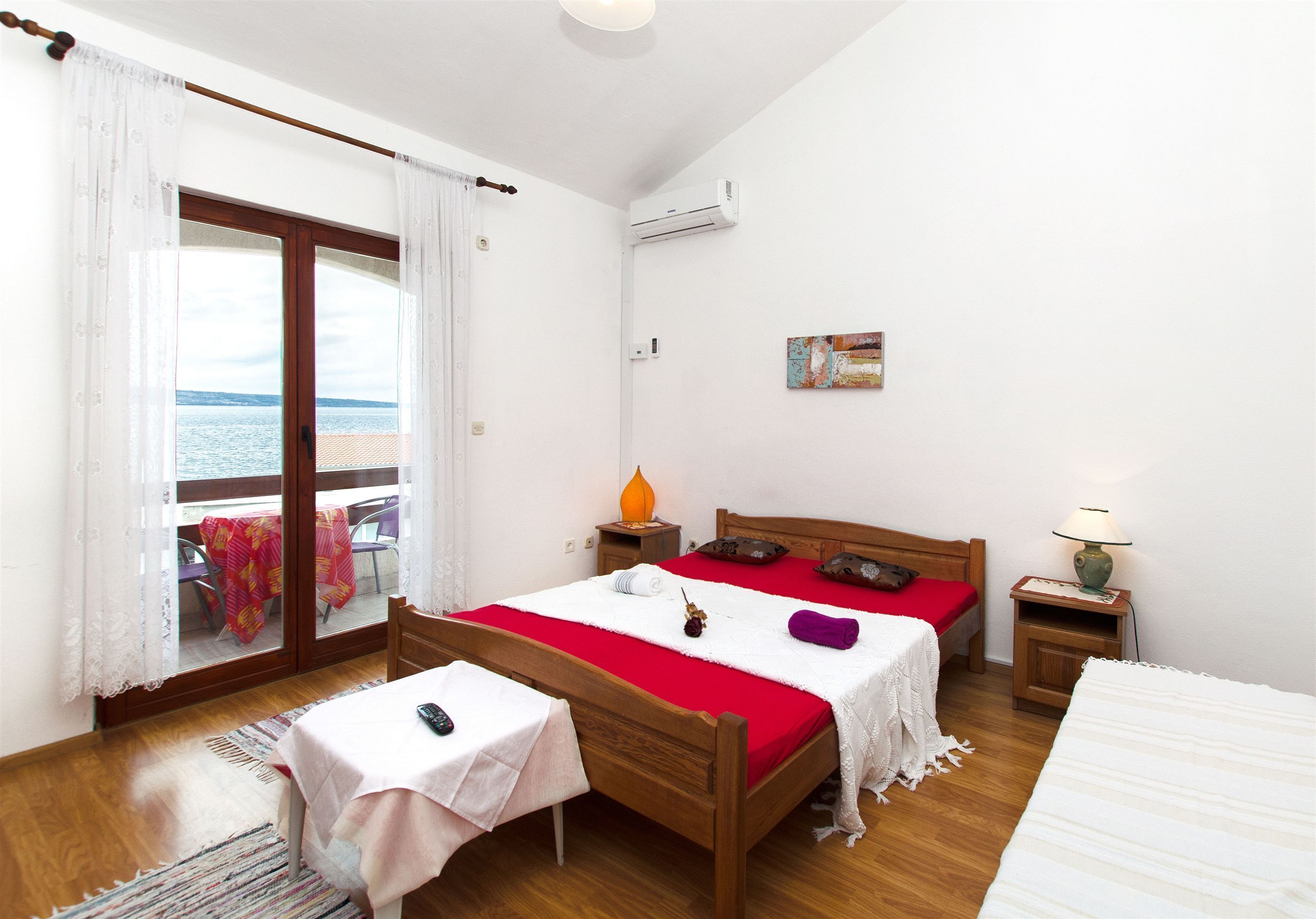 Un dormitorio con cama de madera, una mesita con un control remoto, una mesita de noche con lámpara y vista al mar a través de una puerta corrediza de vidrio.