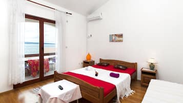 Un dormitorio con cama de madera, una mesita con un control remoto, una mesita de noche con lámpara y vista al mar a través de una puerta corrediza de vidrio.