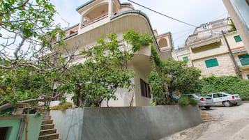 Un edificio residencial con una escalera que lleva a un balcón, rodeado de vegetación y coches aparcados.