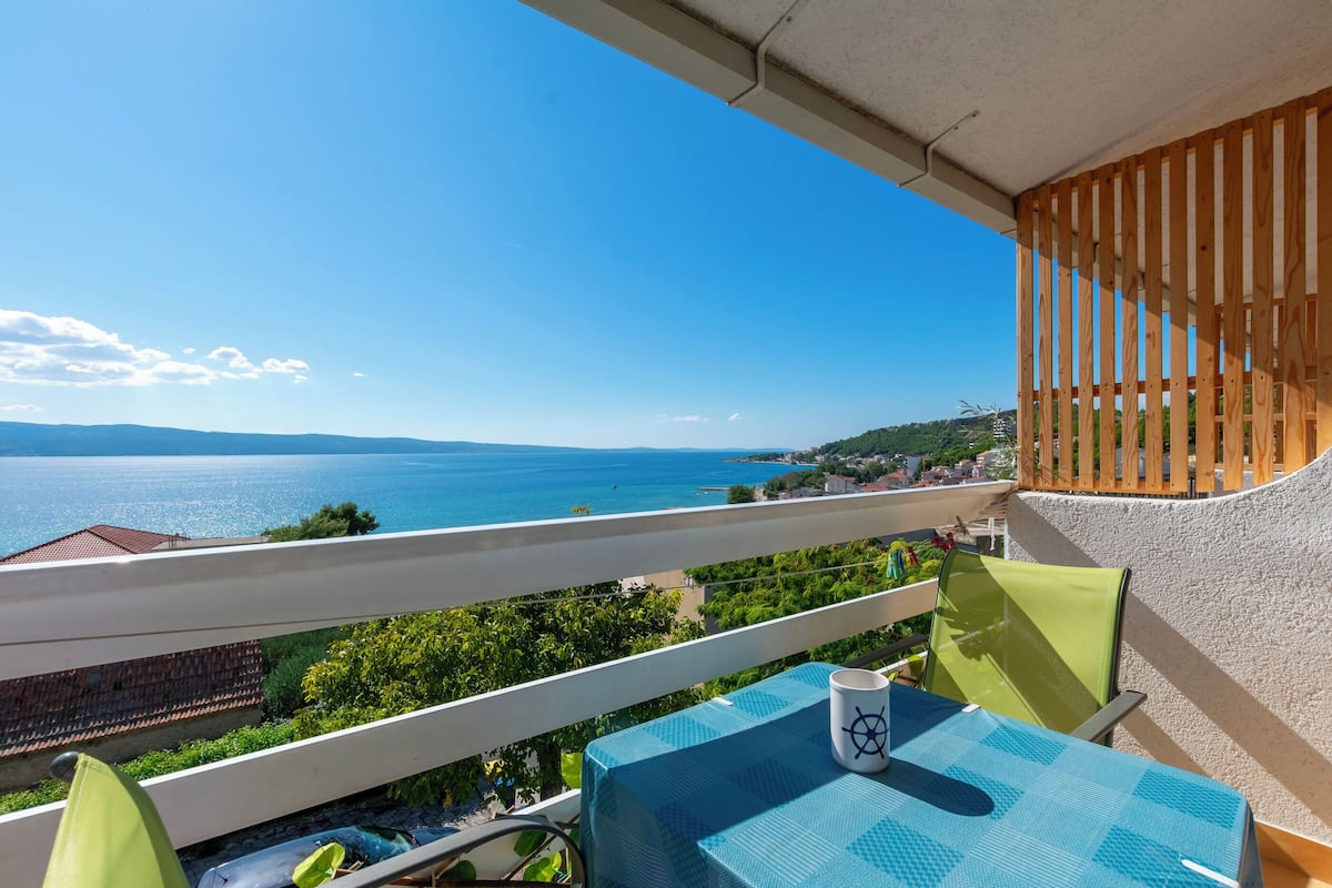 Ein Balkon mit Meerblick, einem Tisch und einem Stuhl sowie einem Holzgeländer.