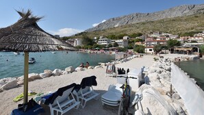 A beach with white lounge chairs, a thatched umbrella, and a sign advertising a ski resort. - Apartments Boro (Dugi Rat)