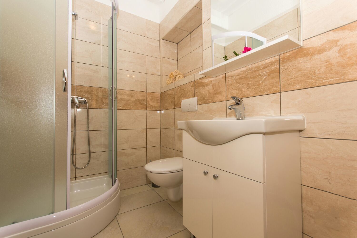 A bathroom with a glass-enclosed shower, a white toilet, and a beige vanity with a sink.
