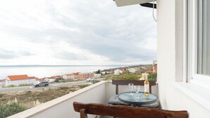 En balkon med havudsigt, et bord med to vinglas og en stol med hynder.