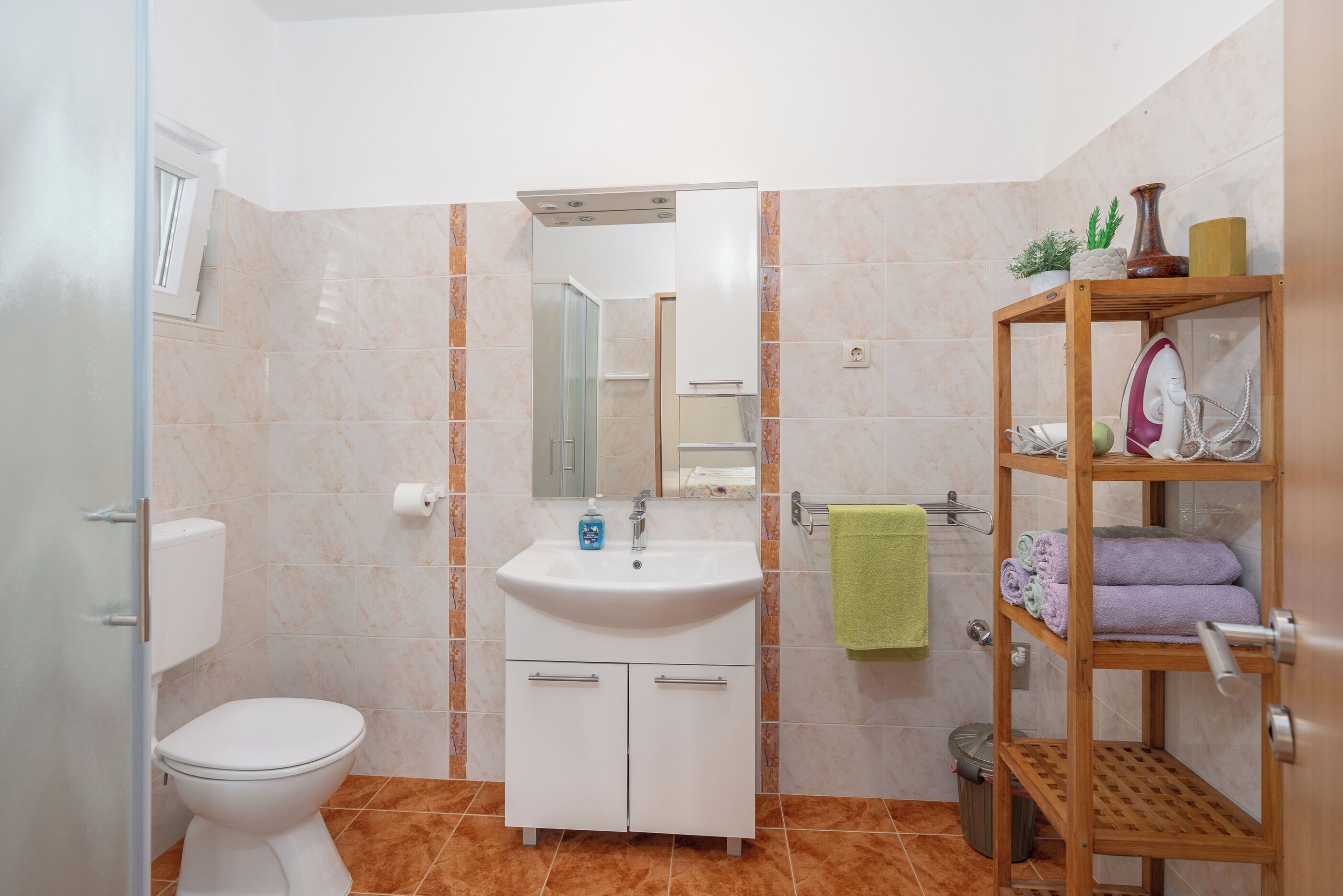 A bathroom with a toilet, sink, mirror, and a wooden shelf with towels.