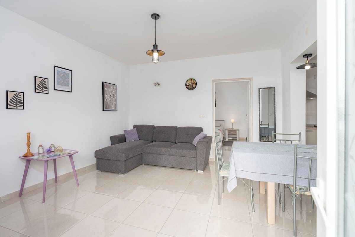 Una sala de estar moderna con un sofá seccional gris, una mesita morada, una mesa de comedor con sillas y un espejo grande.