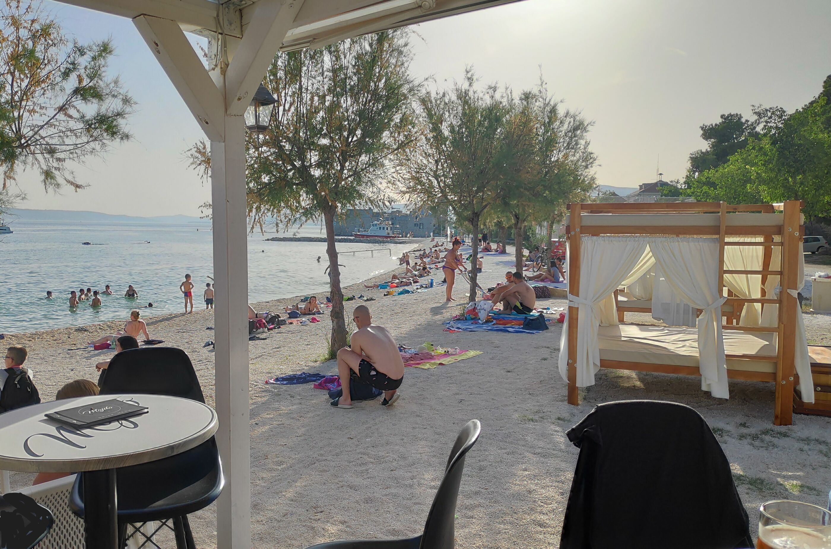 Een strandsetting met een overdekte zithoek, een houten schommel en uitzicht op de zee.