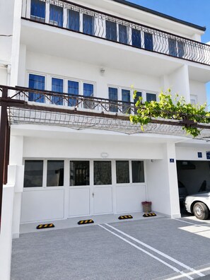 A two-story building with a white facade, a covered parking area, and a white car parked inside. - Apartment Gordana (Kastela)