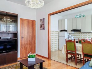 Una sala de estar con televisor, un aparador de madera, una mesa con un florero y un comedor con mesa y sillas.