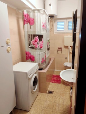 Ein kleines Badezimmer mit Waschmaschine, Duschkabine mit rosa Blumen, Toilette und Waschbecken.