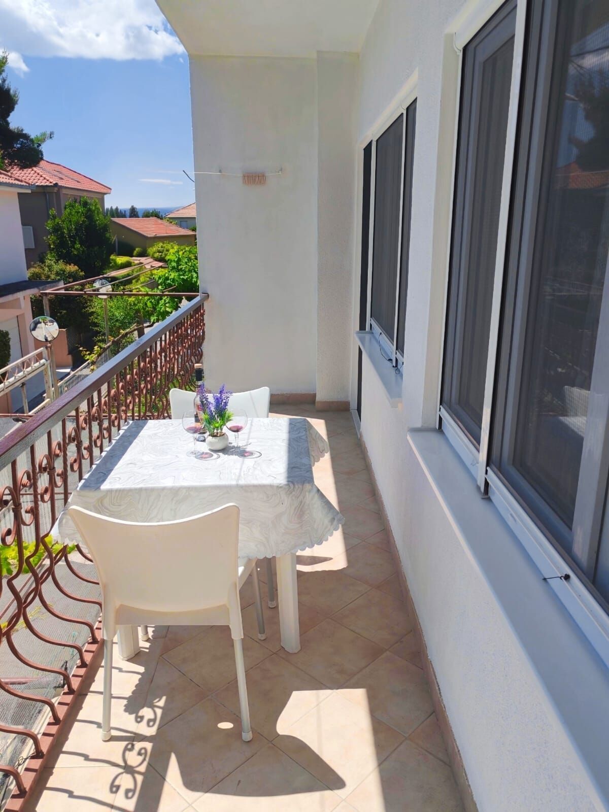 Uma varanda com mesa e cadeiras, um vaso de planta e vista para o bairro.