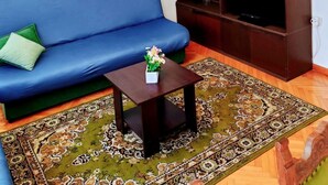 A living room with a blue sofa, a wooden entertainment unit, a chandelier, and a patterned rug. - Apartment Gordana (Kastela)