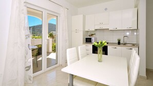 A modern kitchen with white cabinets, a dining table with chairs, and a view of a balcony with a mountain backdrop. - House Pazanin (Marina)