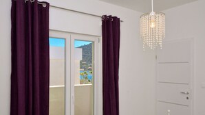 A room with a sliding glass door leading to a balcony, white walls, and a chandelier. - House Pazanin (Marina)