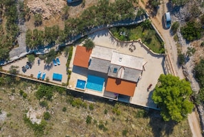 An aerial view of a property with a swimming pool, a covered patio, and a road leading to a parked car. - House Kristiana (Supetar)