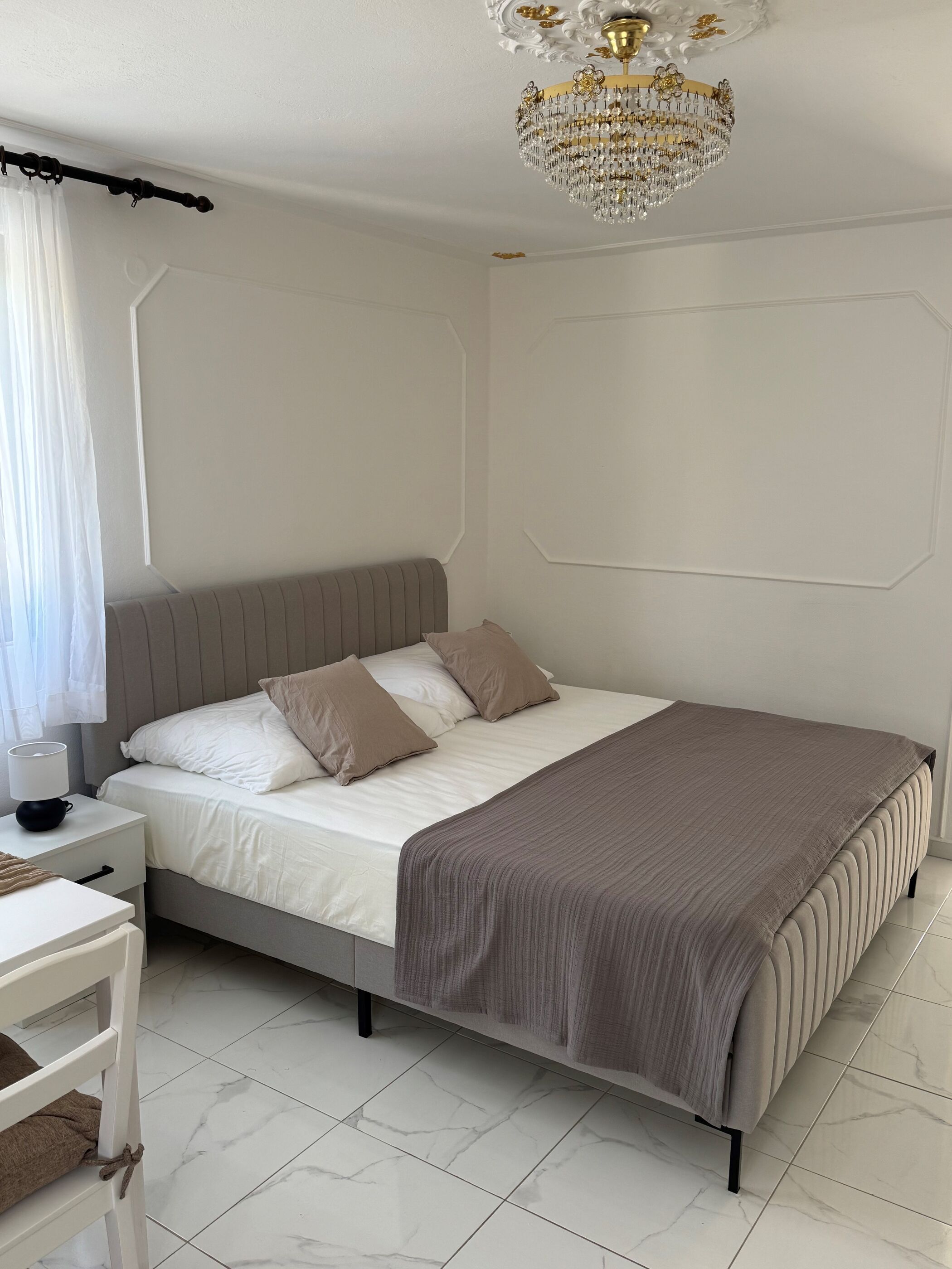 Een slaapkamer met een bed, nachtkastje, lamp en een kroonluchter.