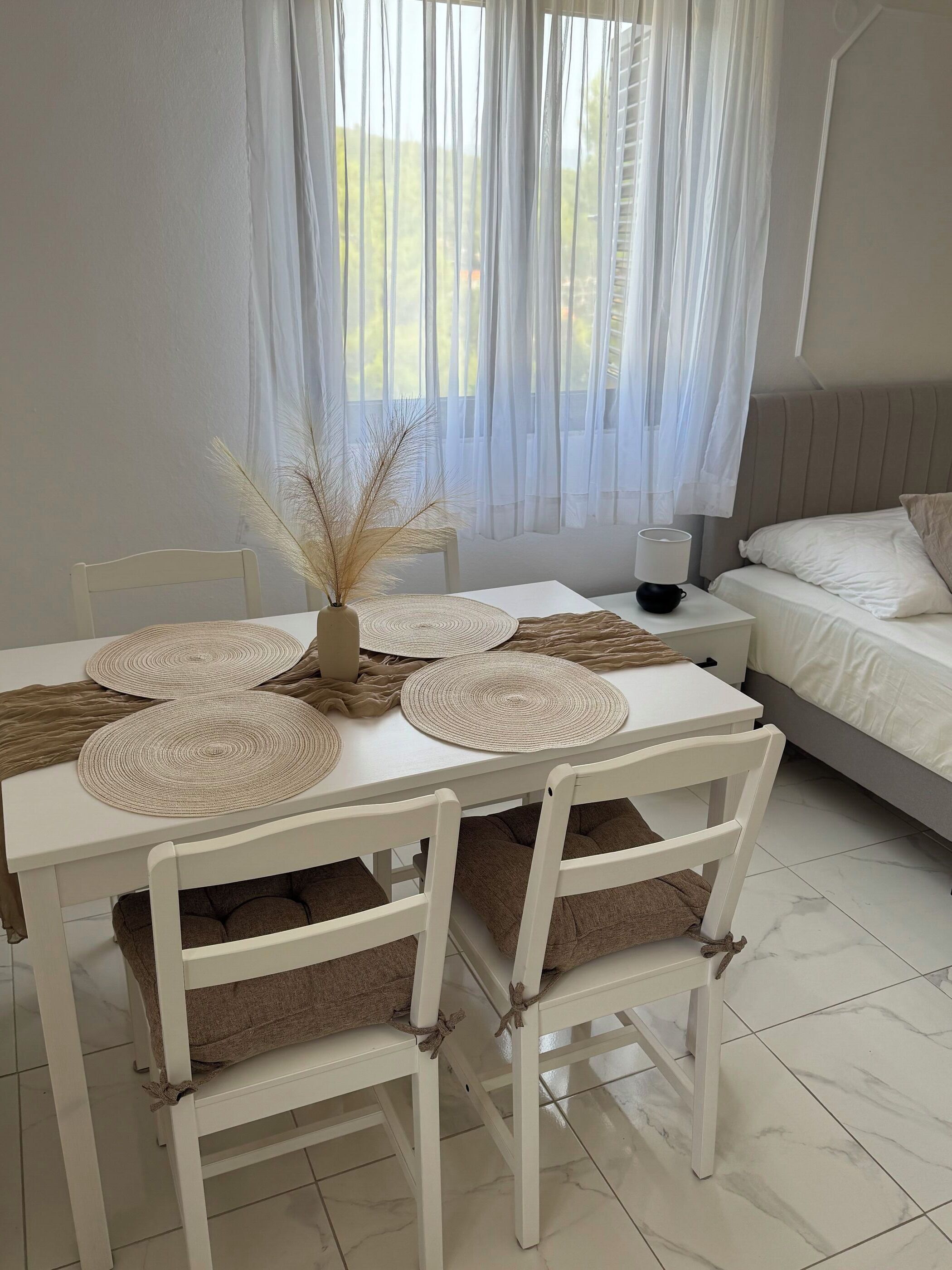 A room with a dining table set with placemats, chairs, and a vase with dried plants.