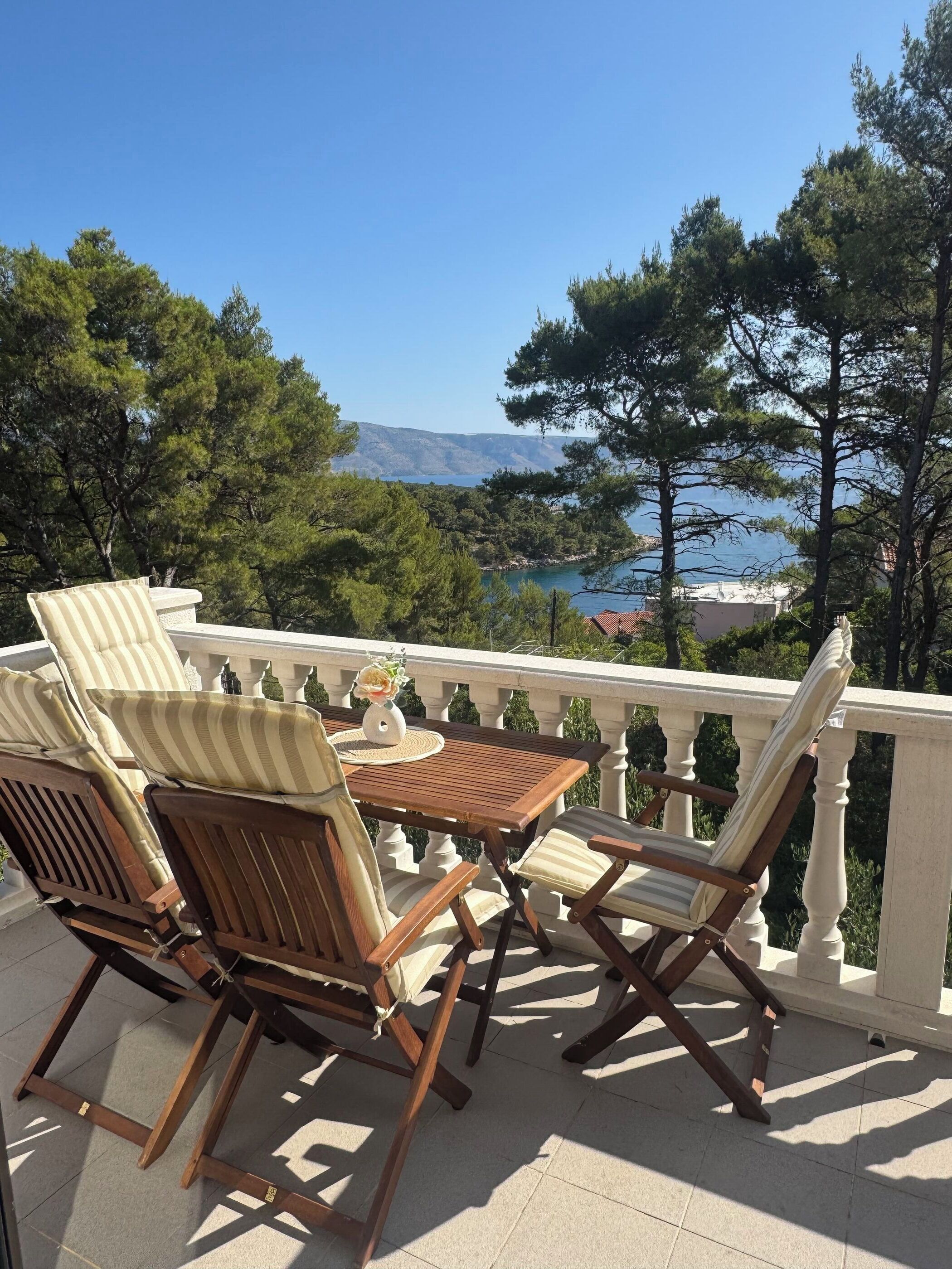 A wooden outdoor seating area with a table and chairs, overlooking a scenic landscape with trees and a body of water.
