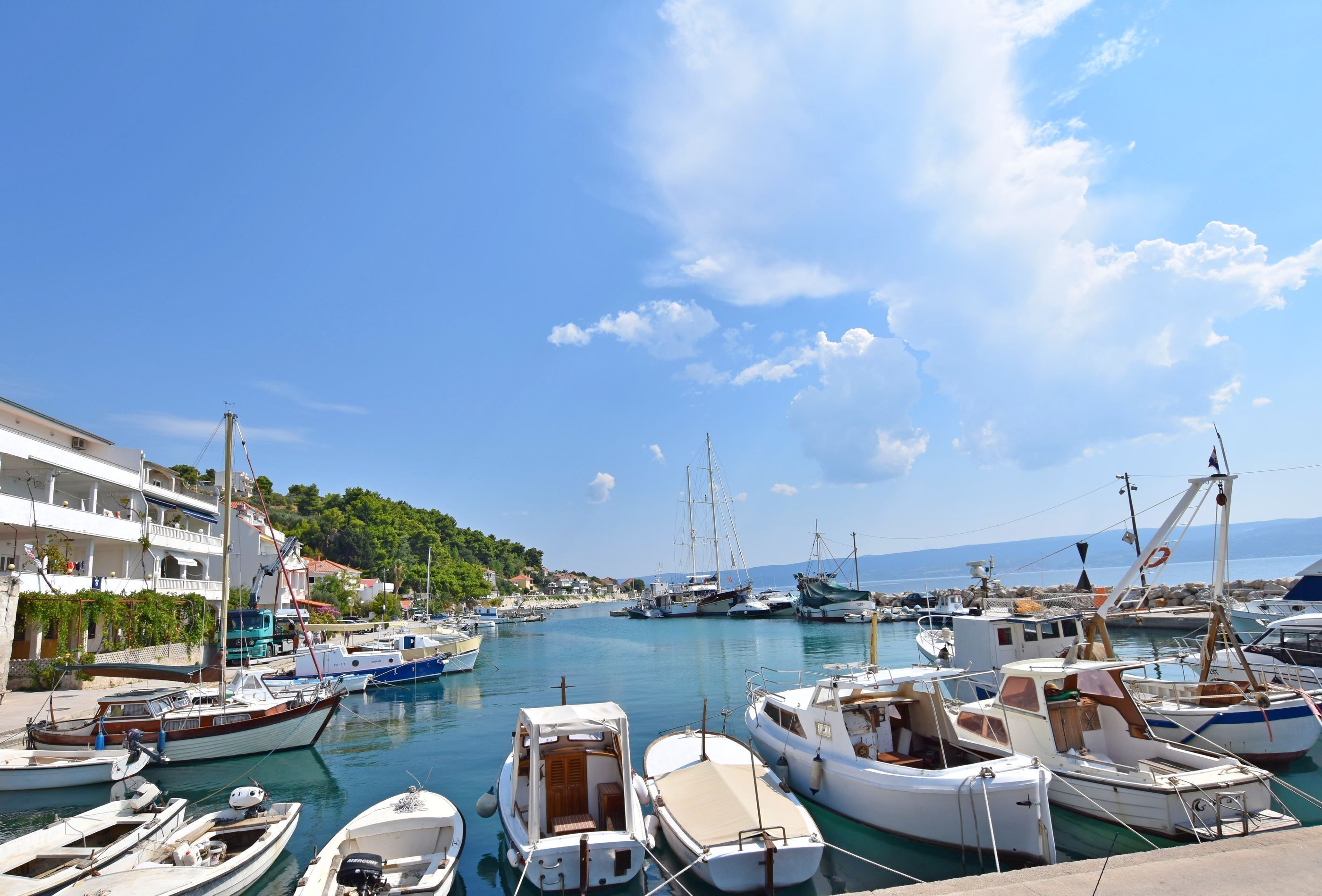 A marina with various boats docked, a clear sky, and buildings along the waterfront.