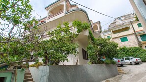 Un edificio residencial con una escalera que lleva a un balcón, rodeado de vegetación y coches aparcados.