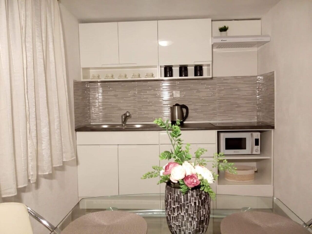 Eine moderne Küche mit weißen Schränken, einer Edelstahl-Spüle, einer Mikrowelle und einer Dekovase mit Blumen auf der Arbeitsplatte.