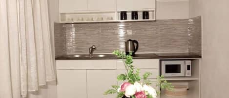 A modern kitchen with white cabinets, a stainless steel sink, a microwave, and a decorative vase with flowers on the counter.
