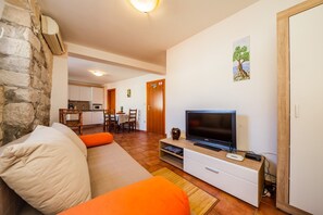 A living room with a sofa, TV, and a stone wall. - Apartments Villa Mirakul (Kastela)