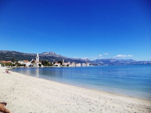 Eine Küstenstadt mit Sandstrand, einer markanten Kirche und Bergen im Hintergrund.