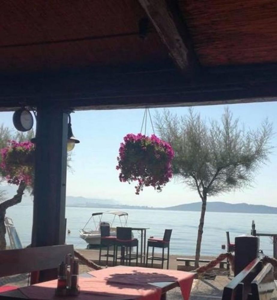 An outdoor seating area with tables and chairs, overlooking a body of water and a distant mountain range.