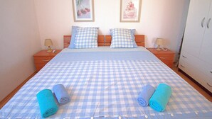 A bedroom with a checkered bedspread, two pillows, two bedside tables with lamps, and a wardrobe. - Apartment Zita (Rogoznica)