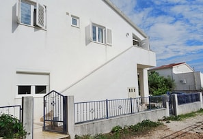 A white building with a gated entrance, a staircase, and a blue metal fence. - Apartment Zita (Rogoznica)