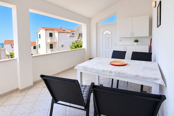 A small dining area with a table and chairs, a view of buildings through a window, and a door leading to a kitchen. - Apartment Zita (Rogoznica)
