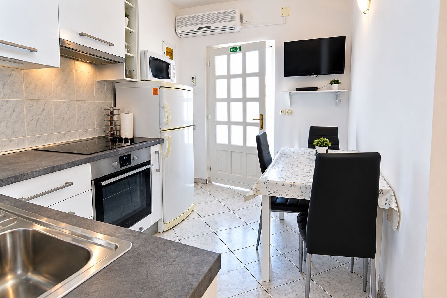 Une cuisine compacte équipée d’un four encastré, d’un four à micro-ondes et d’un coin repas avec une table et des chaises.