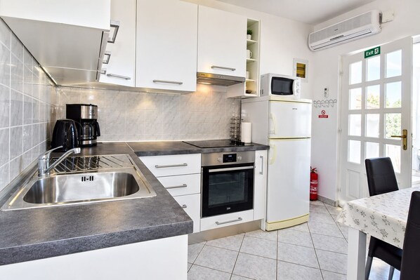 Cozinha moderna com forno embutido, micro-ondas e pia. Há uma mesa de jantar com cadeiras e um extintor de incêndio na parede.