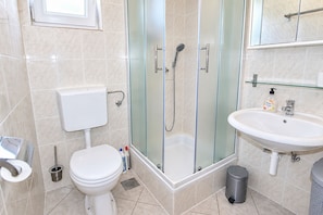 A bathroom with a toilet, a glass-enclosed shower, a sink, and a trash bin. - Apartment Zita (Rogoznica)