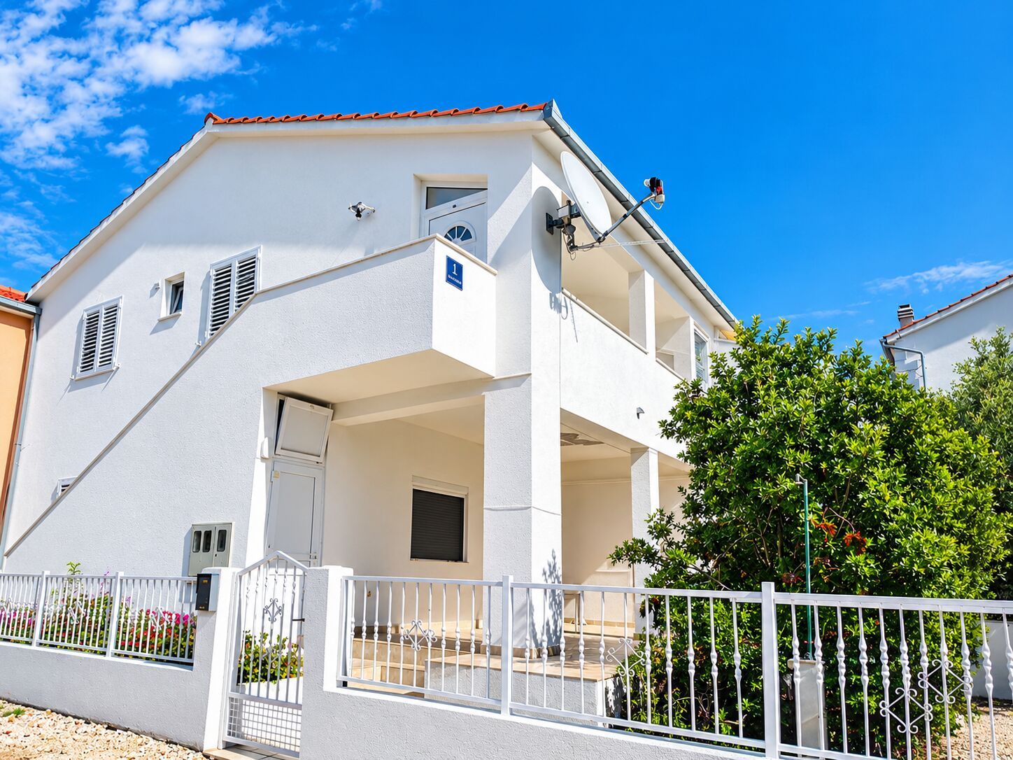 A two-story building with a balcony, a satellite dish, and a white fence.