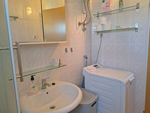 A bathroom with a sink, mirror, glass shelves, a shower, and a washing machine. - Apartment Zita (Rogoznica)