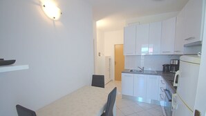 A compact kitchen with white cabinets, a dining table with chairs, a built-in oven, and a coffee maker. - Apartment Zita (Rogoznica)