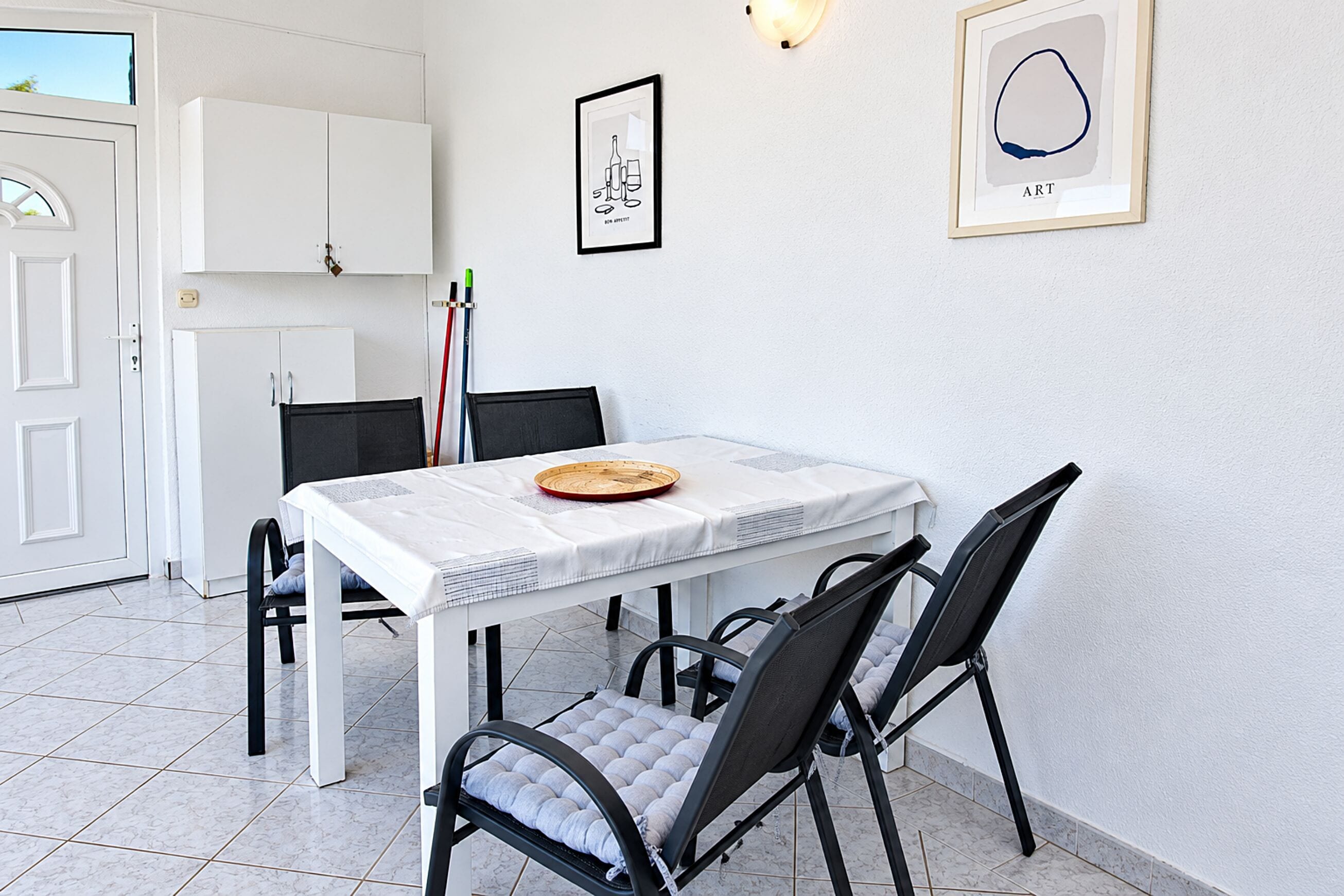 A dining area with a white table, black chairs, a white cabinet, and two framed artworks on the wall.