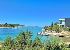A coastal view with clear blue water, boats, and a modern building with a balcony overlooking the sea. - Apartment Zita (Rogoznica)