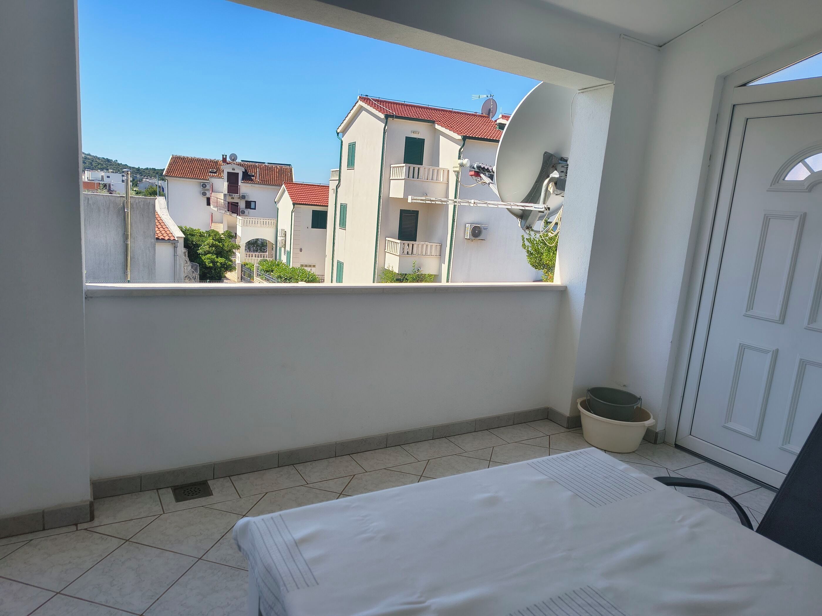 Un balcón con vista a edificios, una cama, una silla y una planta en maceta.