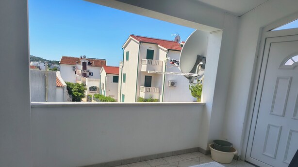 A balcony with a view of buildings, a bed, a chair, and a potted plant. - Apartment Zita (Rogoznica)