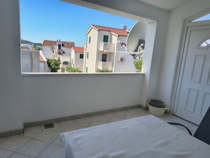 A balcony with a view of buildings, a bed, a chair, and a potted plant. - Apartment Zita (Rogoznica)