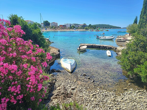 A coastal scene with boats, rocky shore, and buildings in the background. - Apartment Zita (Rogoznica)