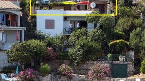 A coastal property with a stone staircase leading to a balcony, a small boat docked in the water, and a clear view of the sea. - Apartments Roko (Primosten)