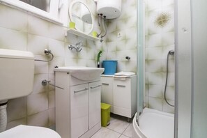 Un baño con inodoro, lavabo, espejo, ducha y un pequeño cubo de basura.